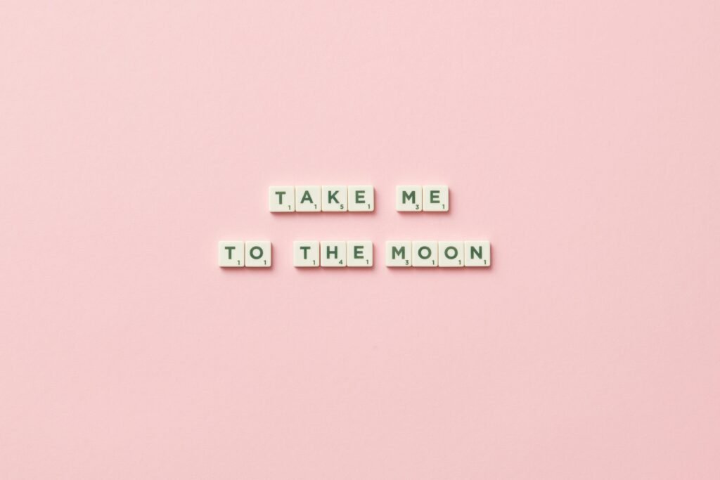 Scrabble letters arranged to say 'Take Me to the Moon' on a pink background.
